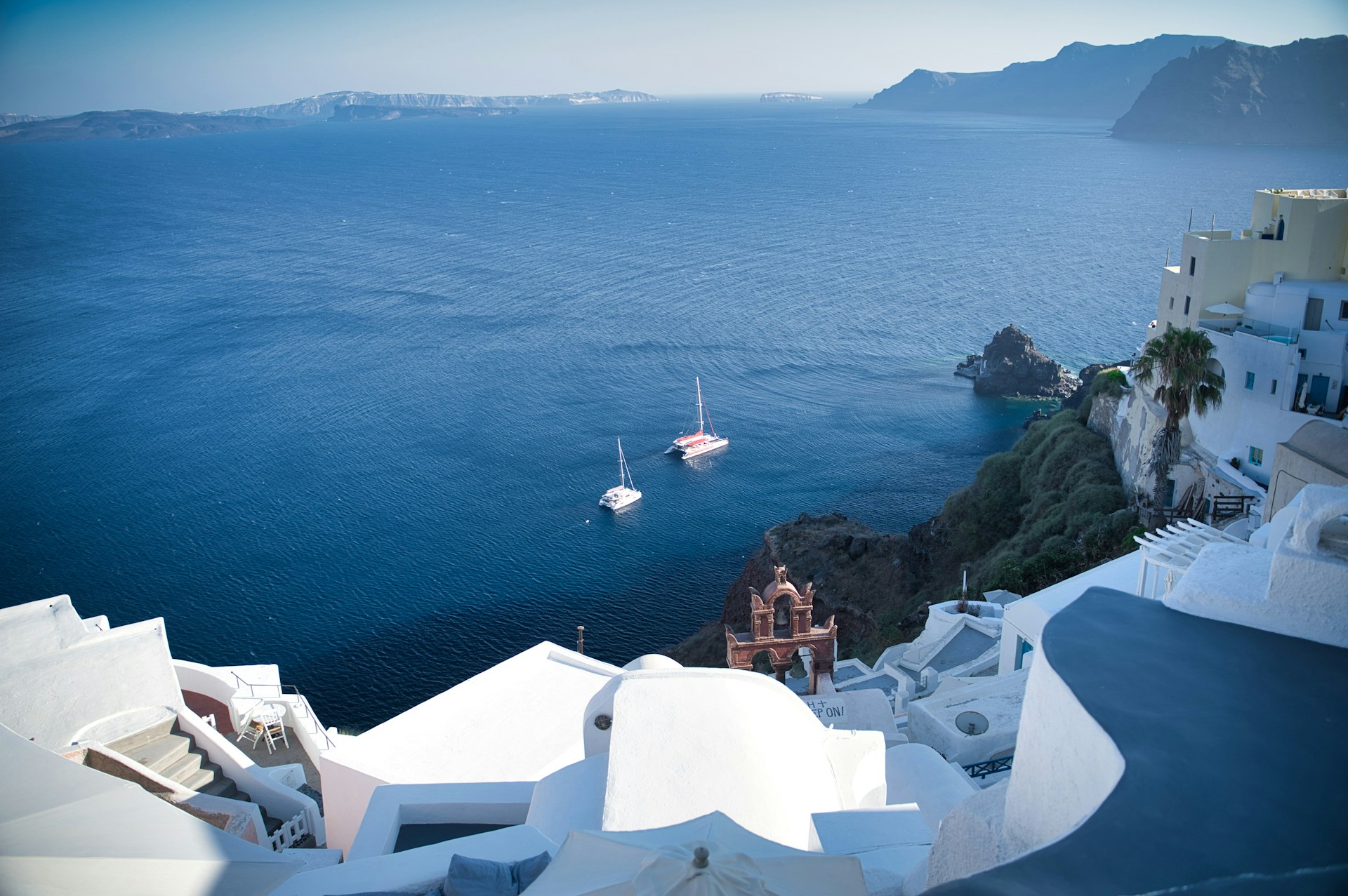 Panoramic views of white-washed buildings perched on the caldera cliffs and the dark-blue Aegean Sea in the background